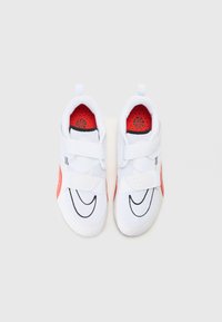 Chaussures de sport blanches avec une tige en maille, des accents noirs, un intérieur rouge et des sangles auto-agrippantes. Présente un logo bien visible sur le côté.