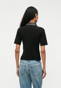 Melna ribota īsām piedurknēm tops ar teksturētu apkakli, kas rotāta ar sudraba kniedēm. Apvienots ar gaismas zilām augsto jostasvietu džinsu biksēm.