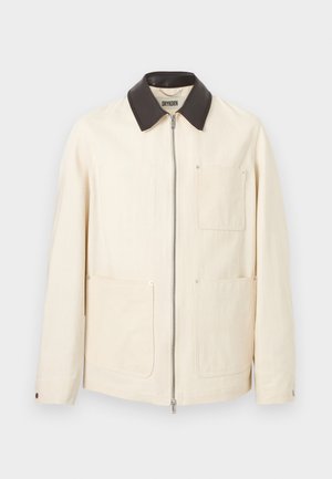 Kremowa kurtka z czarnym kołnierzem, przednim zamkiem błyskawicznym oraz trzema dużymi naszywanymi kieszeniami, dwie na dole i jedna na piersi.