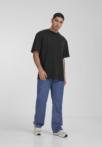 Svart bomulls t-skjorte med korte ermene, rund hals, og avslappet passform, kombinert med blå denim jeans og kremfargede sneakers.
