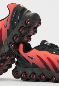 Baskets Nike avec une tige en mesh rouge et noir, semelle en caoutchouc noire dotée de coussins d'air visibles et accents métalliques sur le logo swoosh.