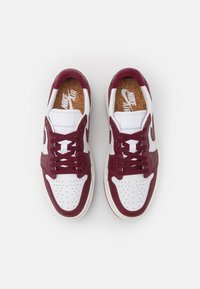 Paire de baskets Nike Air blanches et rouge foncé avec boîte à orteils perforée et semelles intérieures marron, vues de dessus sur fond blanc.