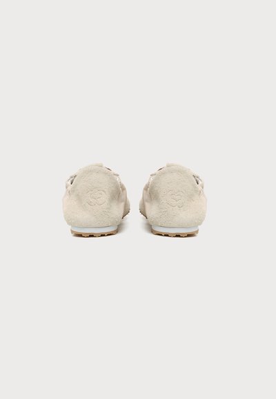 Paire de chaussures casual en daim beige vues de dos avec logos embossés sur les talons et semelles en caoutchouc marron clair.
