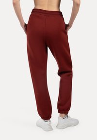 Bordeauxfarvede sweatpants lavet af blødt stof, med elastisk talje og manchetter, parret med hvide træningssko. Enkel og funktionel design.