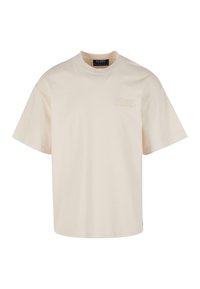 Beige kokvilnas T-krekls ar īsām piedurknēm, apaļu apkakli un vizuāli smalku emblēmju kreisajā krūtī. Tieša griezuma, minimālisma dizains.