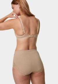 Beige podprsenka a set kalhotek s vysokým pasem. Podprsenka má nastavitelné ramínka a zapínání na háček; kalhotky mají krajkovou šňůrku podél otvorů na nohy.