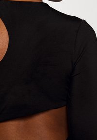 Gros plan du haut du dos et de l'épaule d'une personne portant un haut noir ajusté à manches longues avec un détail découpé.