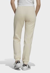 Pantaloni da jogging beige con fascia elastica in vita e polsini, caratterizzati da una leggera texture spazzolata. Abbinati a sneakers bianche con strisce nere.