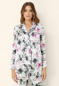 Květinová pyžamová souprava z lehkého materiálu, se vzorem růžových a černých květin na bílém pozadí. Výrazné černé lemování kolem límce a kapsy.
