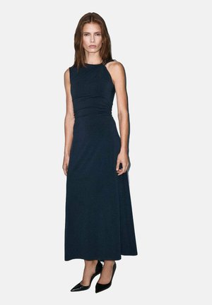 Vestido largo sin mangas de color azul marino con detalle fruncido en la cintura, textura suave y silueta de largo completo, combinado con tacones negros.