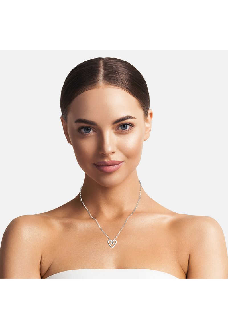 Sömlös silverhalsband med ett hjärtformat hänge, en delikat kedjedesign och glänsande finish, bärs mot en bar axel.