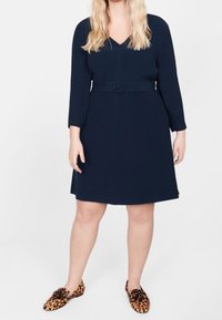 Laivansininen mekko V-aukkolla, kolmen neljänneksen hihoilla, vyötäröllä vyö ja laajenevalla hameella. Yhdistetty leopardikuosisilla liukuva kengillä.