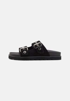 Sandali a scivolo in suede nero con due cinture regolabili in argento, suola in gomma con un motivo texturizzato e design piatto.