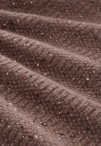 Tissu brun texturé avec un motif en côtes, présentant des éclats de rouge, bleu et crème ici et là. Aspect doux et légèrement pelucheux.