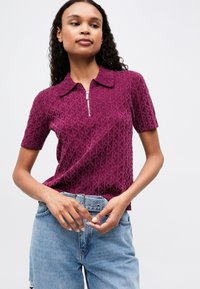 Lühikeste varrukatega, tõmblukuga polo särk tekstureeritud ploomivärvis, millel on rombimuster. Kombineeritud kulunud siniste kõrge vöökohaga teksadega.