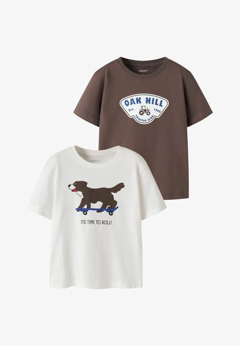 Deux t-shirts enfants à manches courtes : un marron avec "OAK HILL" et un motif de tracteur, un blanc avec un chien sur un skateboard et le texte "IT'S TIME TO ROLL!".