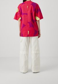 Kortærmet, rød top med store lilla blomster mønstre, parret med hvide cargobukser med lomme detaljer.