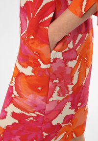 Robe colorée mettant en avant des motifs abstraits vifs en orange et rose, avec un détail de poche sur le côté et une texture douce et soyeuse.