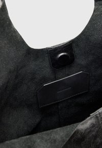 Primo piano dell'interno di una borsa in suede nero che mostra una chiusura a bottone a pressione in pelle e un'etichetta rettangolare in pelle.