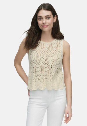 Kanten crop top in crème met ingewikkelde bloemmotieven, gegolfde zoom en mouwloos ontwerp, gecombineerd met witte broek.