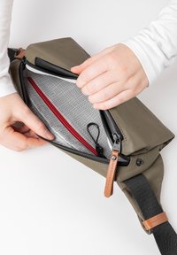 Groene nylon schoudertas met een zwarte schouderband, voorzien van een ritszak, grijze binnenkant en een rode accentzak aan de binnenkant. Detail met leren trekband.