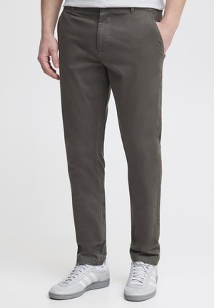Homme portant un pantalon slim kaki avec poches latérales et des baskets blanches sur un fond uni.