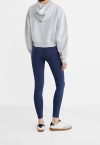 Sudadera gris corta, leggings de punto azul marino y zapatillas blancas con detalles negros. Tejido suave, corte relajado y diseño de pierna ajustada.
