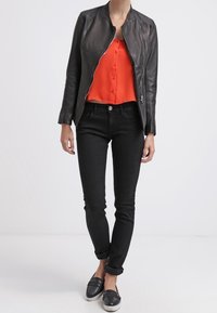 Chaqueta de cuero negra, camisa roja de botones, jeans skinny negros y zapatos negros sin cordones. Textura suave y diseño ajustado.