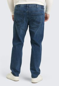 Dunkelblaue Denim-Jeans mit geradem Schnitt, versehen mit Gesäßtaschen und einem dezenten genähten Muster, getragen mit weißen Sneakers.