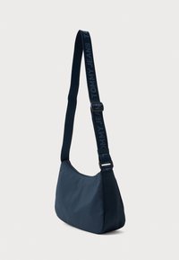 Geantă crossbody de culoare albastru marin cu curea ajustabilă, având textul "TOMMY JEANS", compartiment principal cu fermoar și textură de țesătură netedă.
