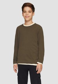 Olijfgroene sweatshirt met lange mouwen en ronde hals, met een contrasterende witte binnenkraag. Gedragen over een wit onderhemd, gecombineerd met marineblauwe broek.