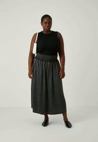 Top preto sem mangas com decote redondo, combinado com uma saia cinza plissada de cintura alta. Modelo usa sapatos pretos planos e segura uma bolsa branca.