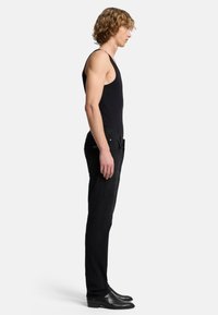 Schwarzes Tanktop mit tailliertem Design, kombiniert mit schmalen schwarzen Jeans. Die Jeans haben einen Standardbund und Seitentaschen. Schwarze Stiefel runden das Outfit ab.