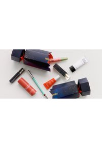 Due scatole di imballaggio blu scuro con decorazioni dorate, circondate da vari prodotti cosmetici in tonalità di rosa, arancione e verde.