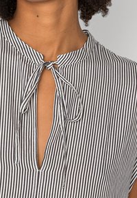 Zwart-wit gestreepte shirt met een striksluiting bij de hals, voorzien van een notch kraag en een stoffen textuur die lichtgewicht lijkt.