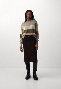 Pull en maille rayé aux couleurs pastel, associé à une jupe midi en velours côtelé marron et à des bottes noires jusqu'aux genoux, présentant une texture subtile et des accents.