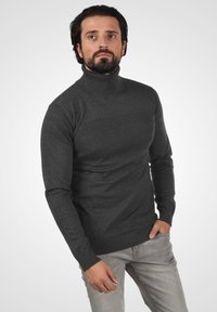 Suéter de cuello alto gris oscuro, tejido de punto, diseño ajustado, cuerpo texturizado, puños acanalados, combinado con jeans gris claro.