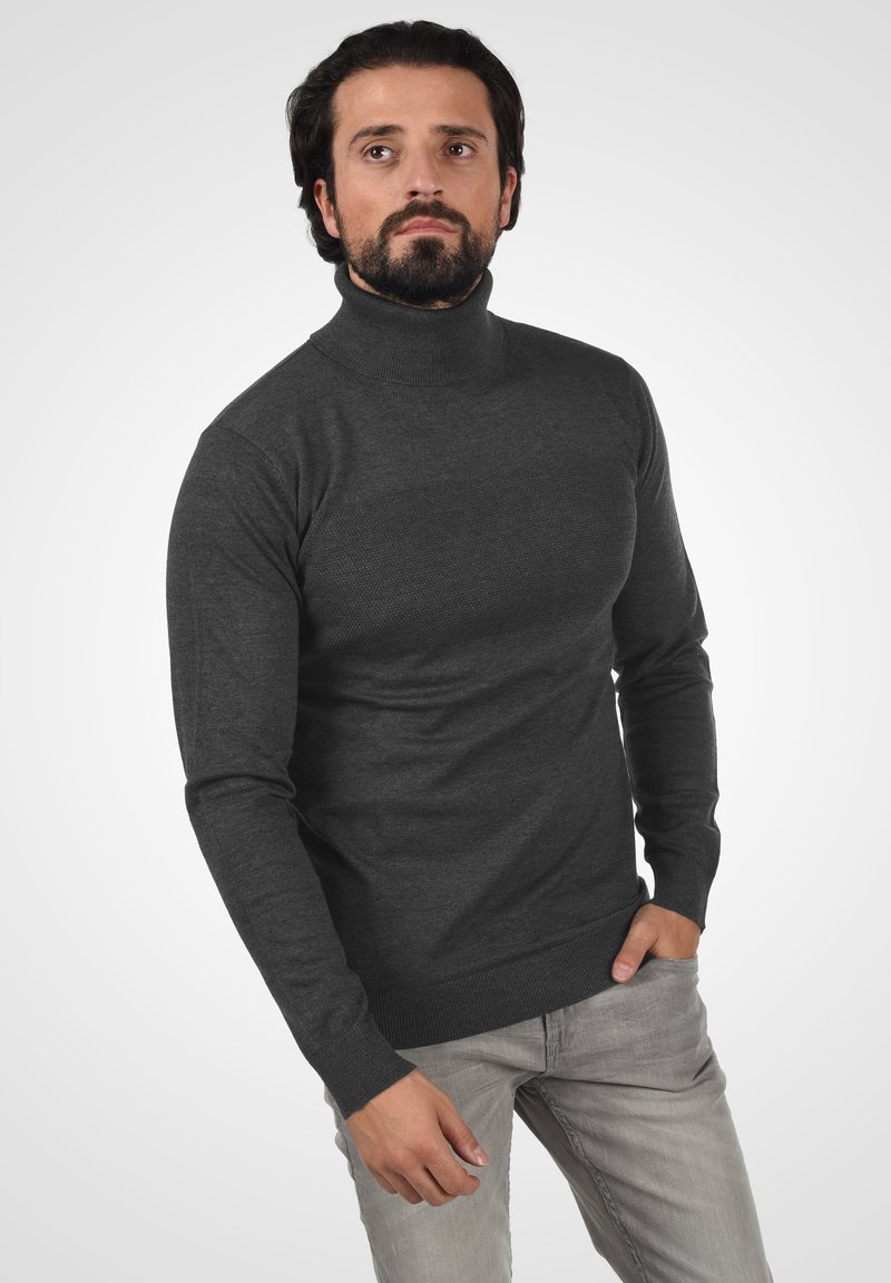 Ciemnoszary sweter typu golf, dzianinowy materiał, dopasowany krój, teksturowane wykończenie, prążkowane mankiety, noszony z jasnoszarymi dżinsami.