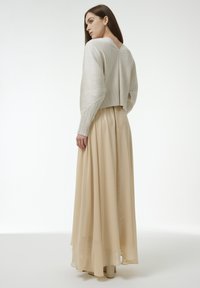 Un pull court texturé gris clair avec des manches longues et un dos en V profond, associé à une longue jupe maxi beige fluide. Tissu lisse et transparent.