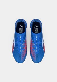 Ein Paar blaue Puma Ultra Fußballschuhe mit roten Streifen und weißen Logos, von oben auf einem weißen Hintergrund betrachtet.