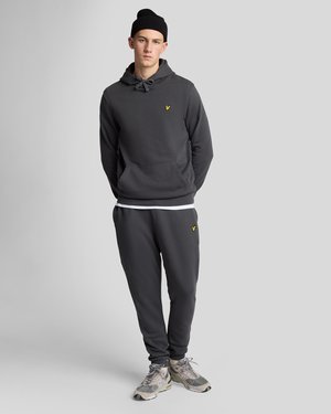 Grijze hoodie met een trekkoord, voorzak en geel logo. Bijpassende grijze joggers met een elastische tailleband. Draagt met sneakers.