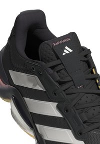 Scarpa sportiva nera con tomaia in mesh texturizzato, accenti grigi, tre strisce sul lato e un collo imbottito per il comfort.
