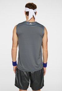 Canotta da uomo grigia con accenti blu, realizzata in tessuto leggero. Presenta una texture a costine e una fascia bianca per la testa. Pantaloni corti neri.