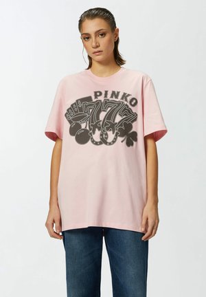 Camiseta de algodón rosa claro con mangas cortas, que presenta una impresión gráfica negra con la palabra "PINKO" y un diseño de tarjeta y trébol.