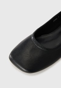 Ballerines noires à bout carrée en cuir texturé, avec une doublure intérieure lisse et un bord cousu simple autour de l'ouverture.