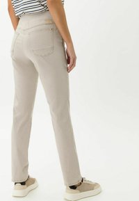 Beige gerade geschnittene Hose mit Gesäßtaschen, kontrastierenden Nähten und hohem Bund, kombiniert mit Sneakers in neutralen Farben.