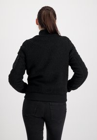Zwarte fleecejas met een gestructureerde, zachte afwerking, geribbelde manchetten en zoom. Voorzien van een ritszak op de linkermouw.