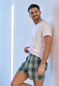 Weißes T-Shirt mit kurzen Ärmeln, kombiniert mit karierten Shorts in Grün und Blau, die über einen elastischen Bund und eine lockere Passform verfügen.