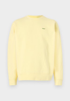 Sweatshirt jaune en coton, avec un col rond et des poignets côtelés. Petit logo vert sur la poitrine gauche. Texture douce et lisse.