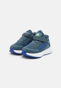 Blauwe sportieve schoenen met een textuur van mesh bovenwerk, voorzien van een strap voor een veilige pasvorm, een ontwerp met drie strepen en een witte tussenzool met blauwe accenten.